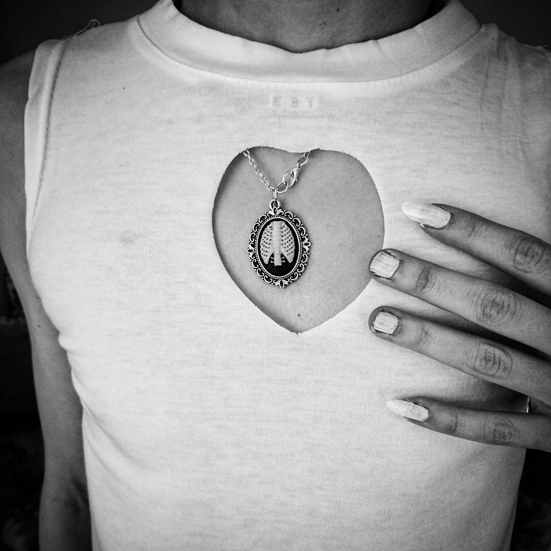 cool Photo of Ryszard Merey's chest, wearing a tshirt with a cutout featuring an abstract pendant.